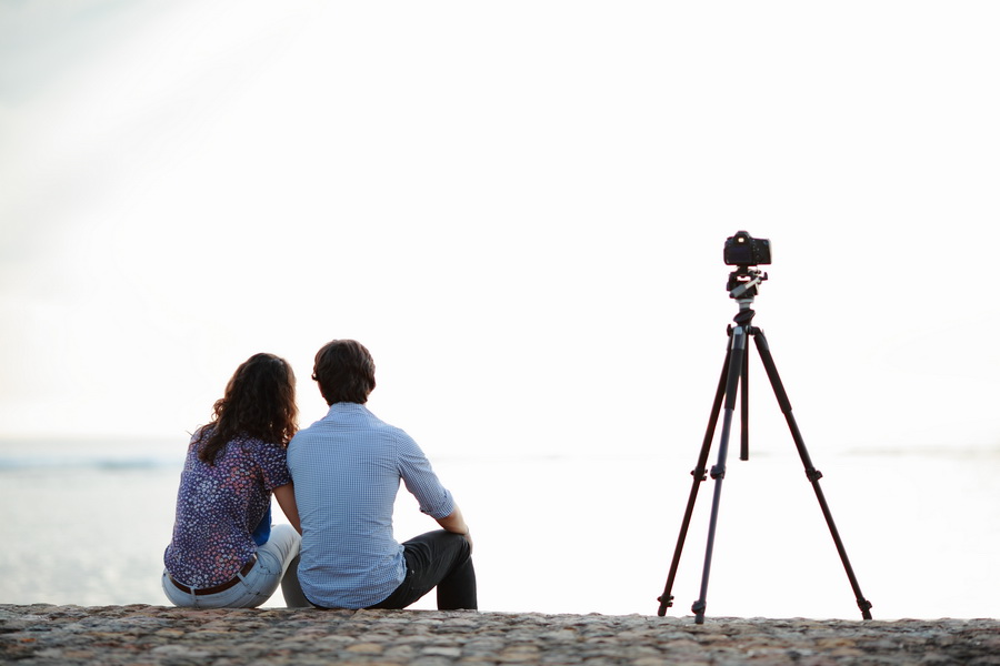 Fotografer prewedding Jakarta konsep candid pasangan duduk di pantai dengan kamera tripod