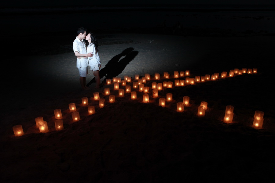 Pasangan berpose romantis di pantai pada malam hari dengan dekorasi lilin untuk sesi foto prewedding bersama fotografer prewedding Jakarta.