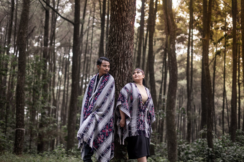 Pasangan mengenakan kain tenun tradisional berjalan di hutan pinus dalam sesi foto prewedding outdoor bersama fotografer prewedding Jakarta.